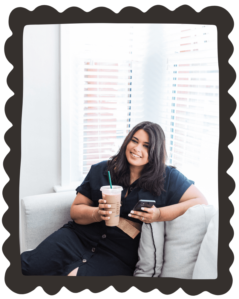 Katrina sat on a cream sofa holding her phone and iced coffee, smiling